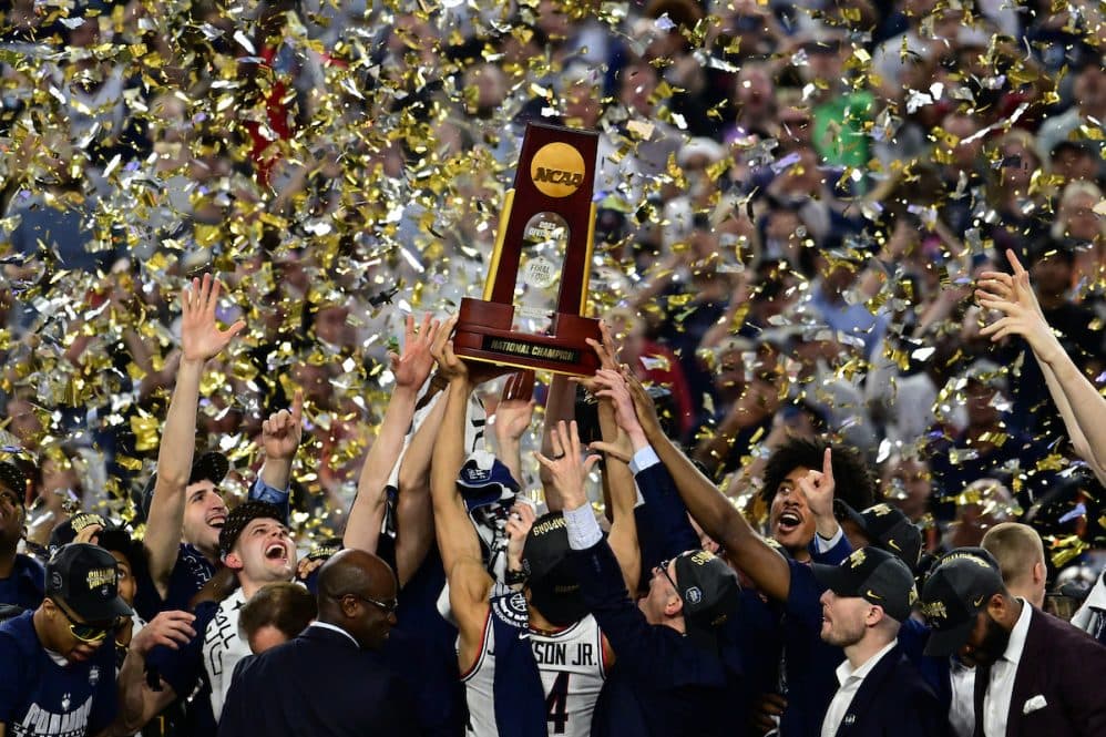 Hands raising the NCAA national championship trophy with confetti
